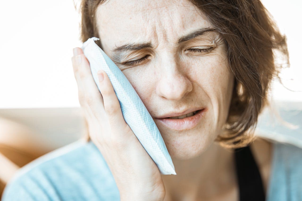 Person holding a cold compress to their cheek to ease tooth pain.